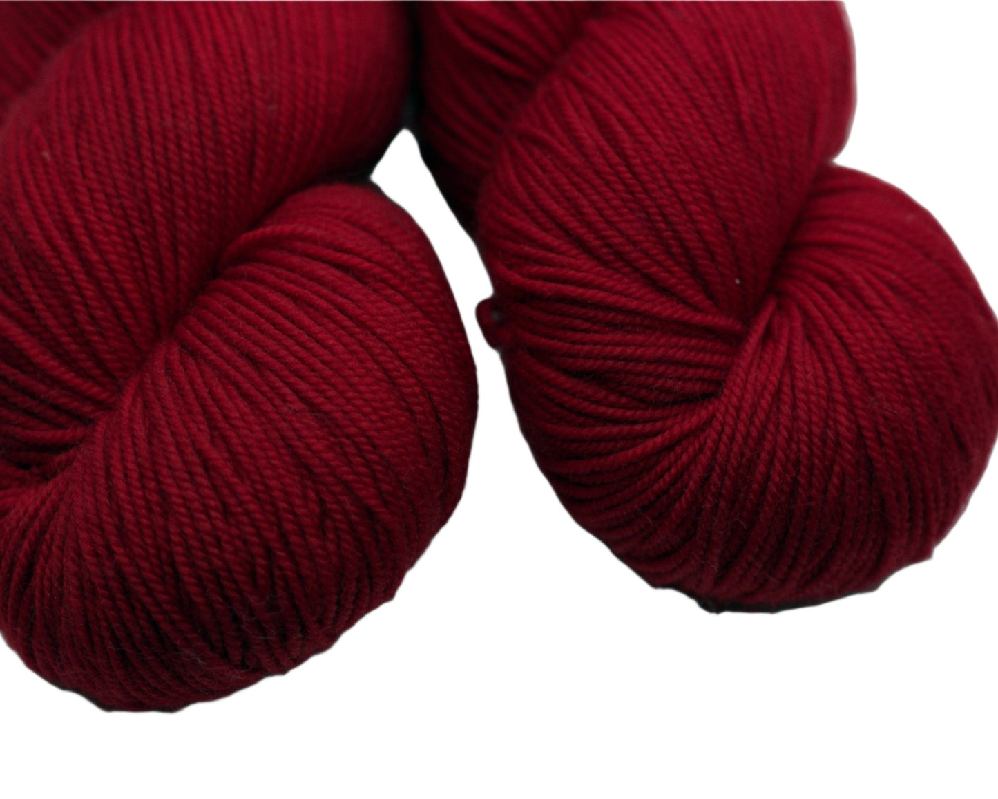 Close up of two twisted skeins lipstick red yarn on white background.
