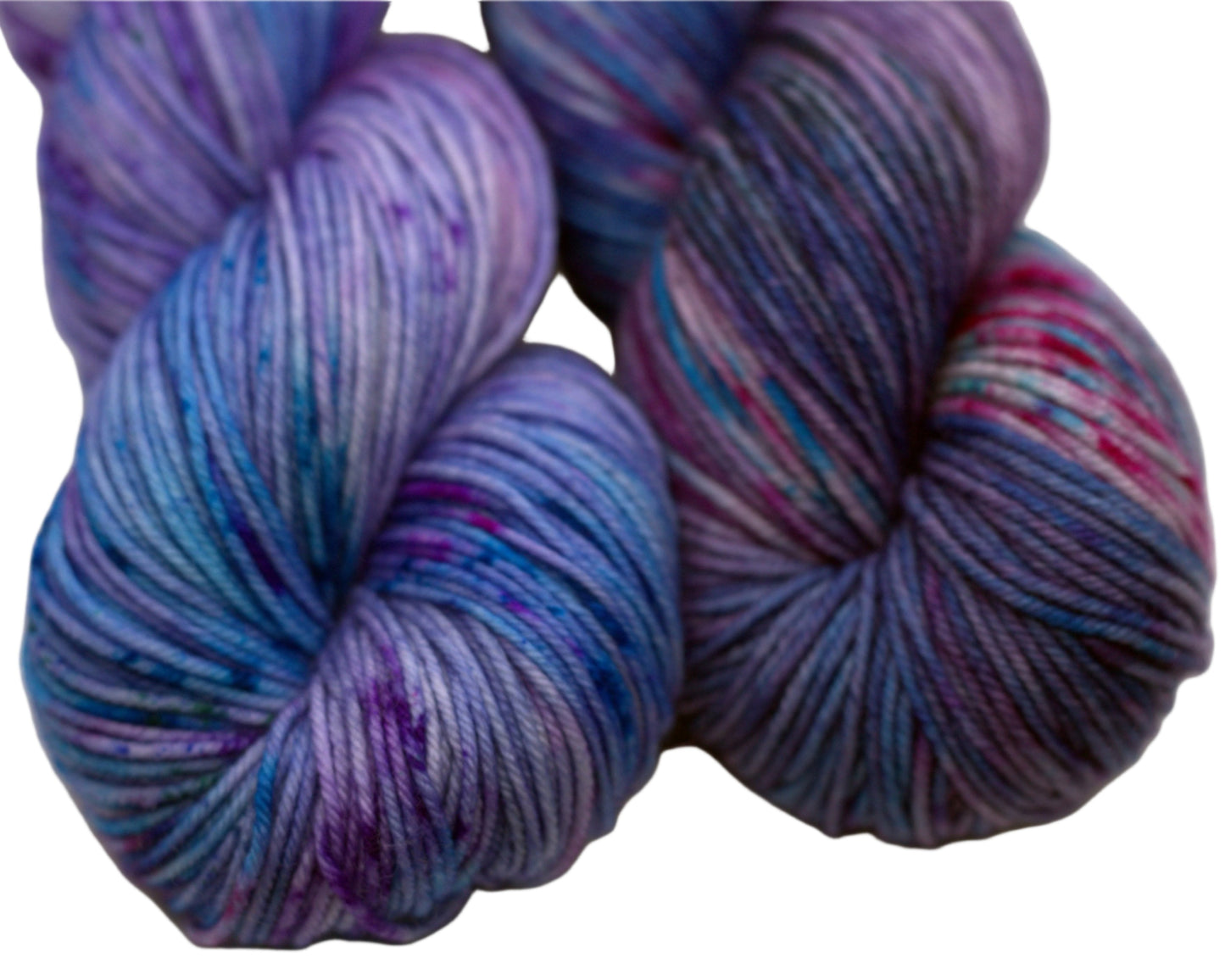 close up of two twisted skeins light purple yarn with turquoise, magenta and black speckles on white background.