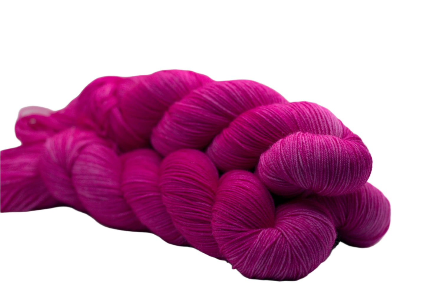 side view of three twisted skeins tonal bright pink yarn on white background.