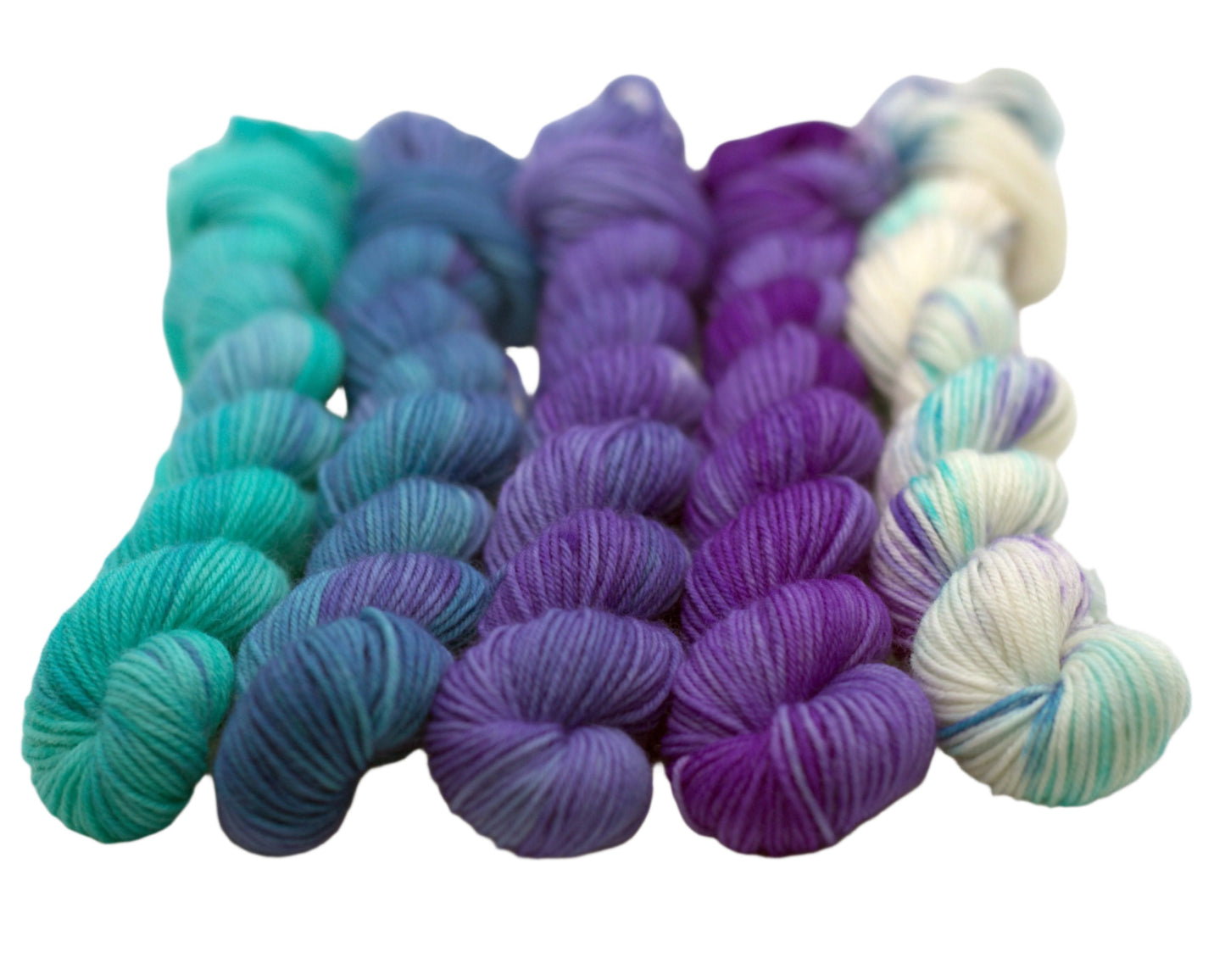 Five mini skeins of aqua to purple gradient twisted yarn on a white background