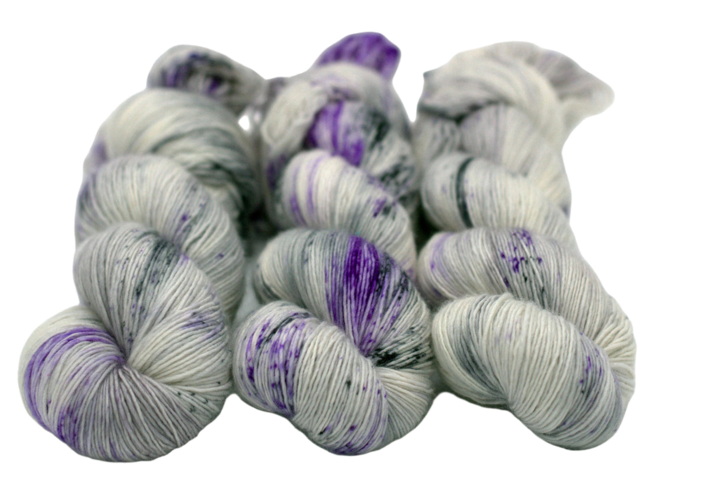 three twisted skeins tonal silver yarn with purple and dark gray speckles on white background.