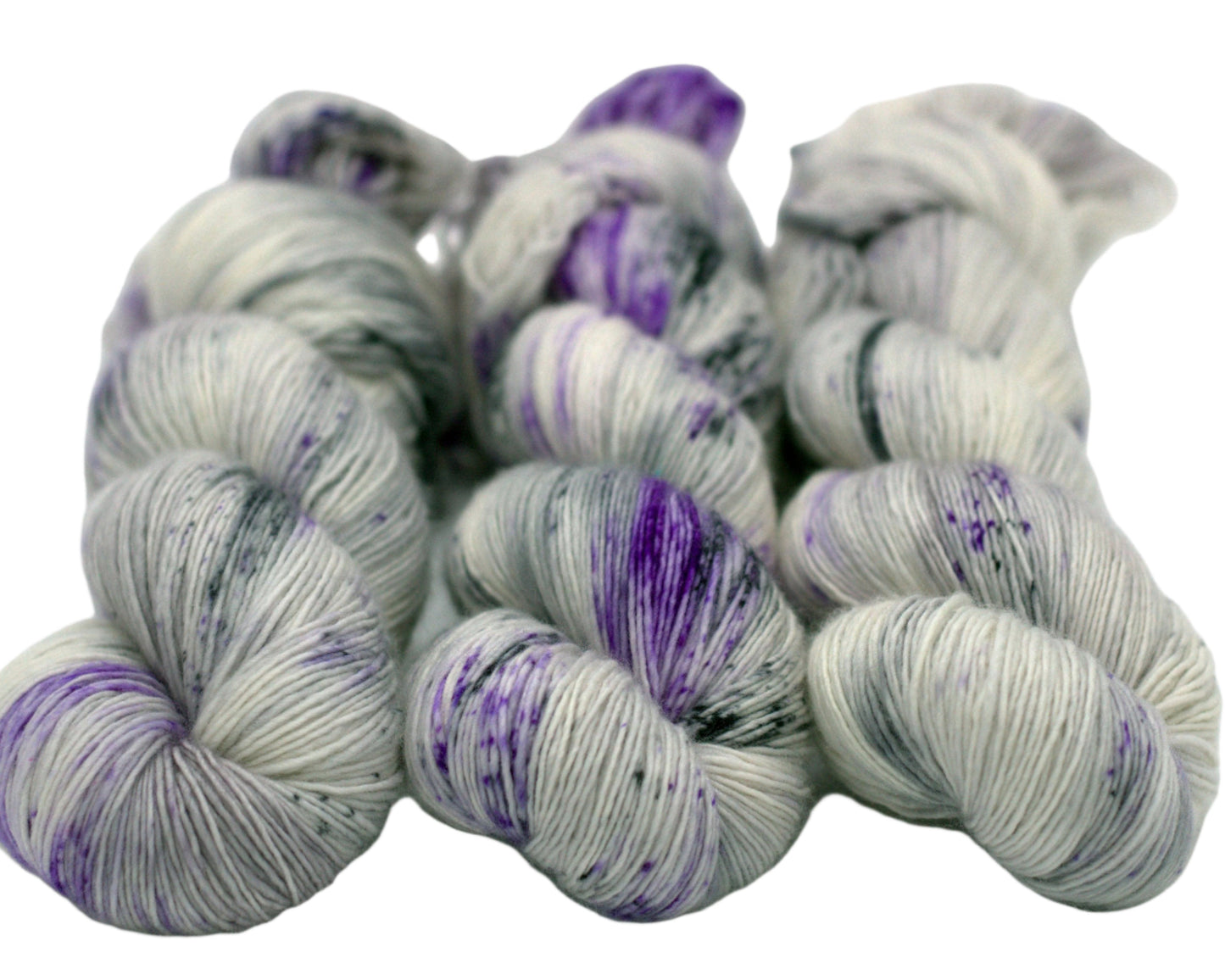 three twisted skeins tonal silver yarn with purple and dark gray speckles on white background.
