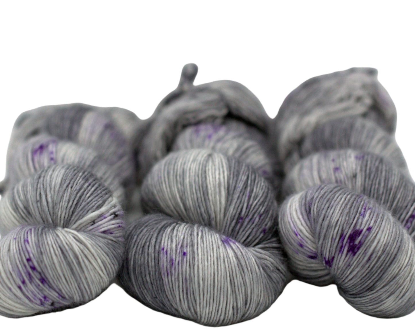 three twisted skeins tonal dark silver yarn with purple speckles on white background.