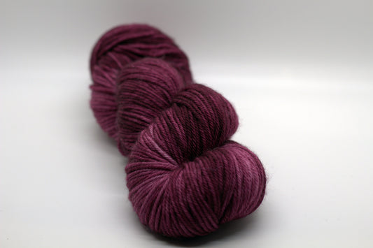 twisted skein tonal red plum colored yarn on white background.