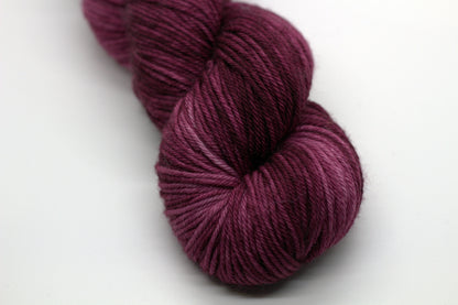 close up twisted skein tonal red plum colored yarn on white background.