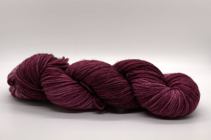 side view of twisted skein tonal red plum colored yarn on white background.
