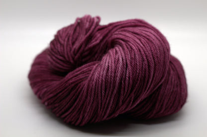 curled up skein of tonal red plum colored yarn on white background.