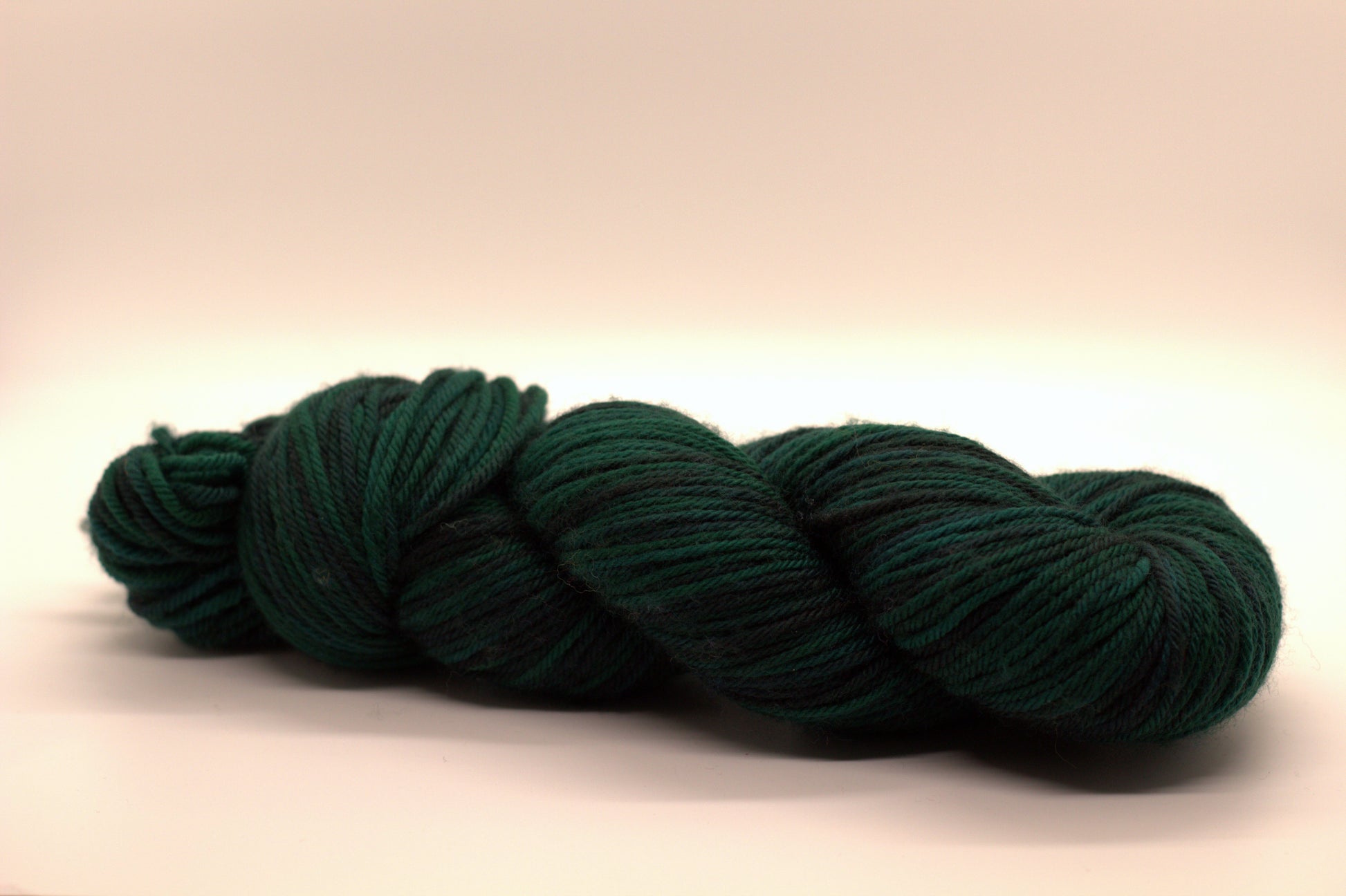 side view of variegated dark green and black yarn on white background.