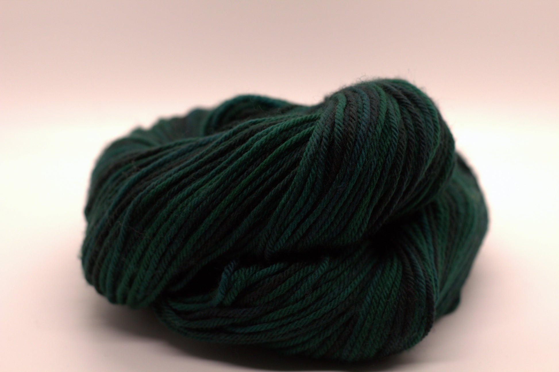 curled up skein variegated dark green and black yarn on white background.