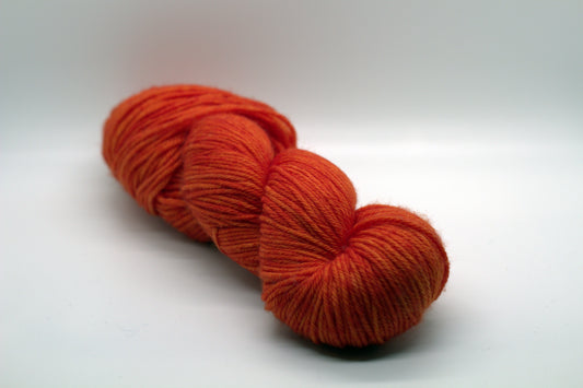 twisted skein of bright orange yarn on white background.