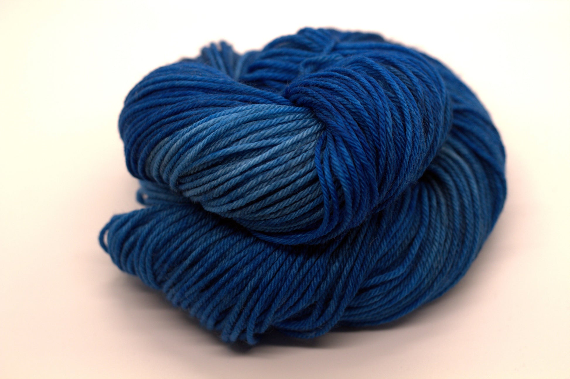 one curled skein tonal peacock blue yarn on white background.