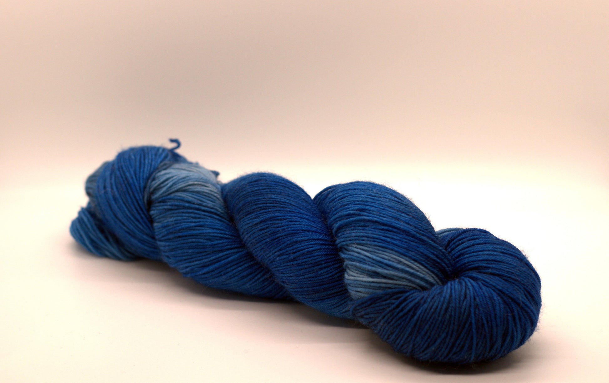 One twisted skein tonal peacock blue yarn on white background.