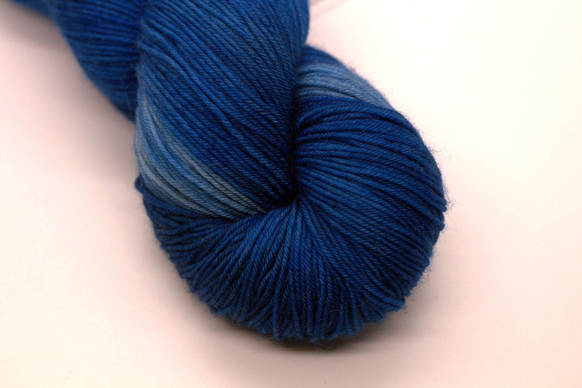 close up of one twisted skein tonal peacock blue yarn on white background.