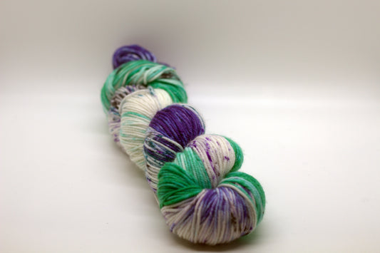 one twisted skein variegated white, green and purple yarn with purple and black speckles on white background.