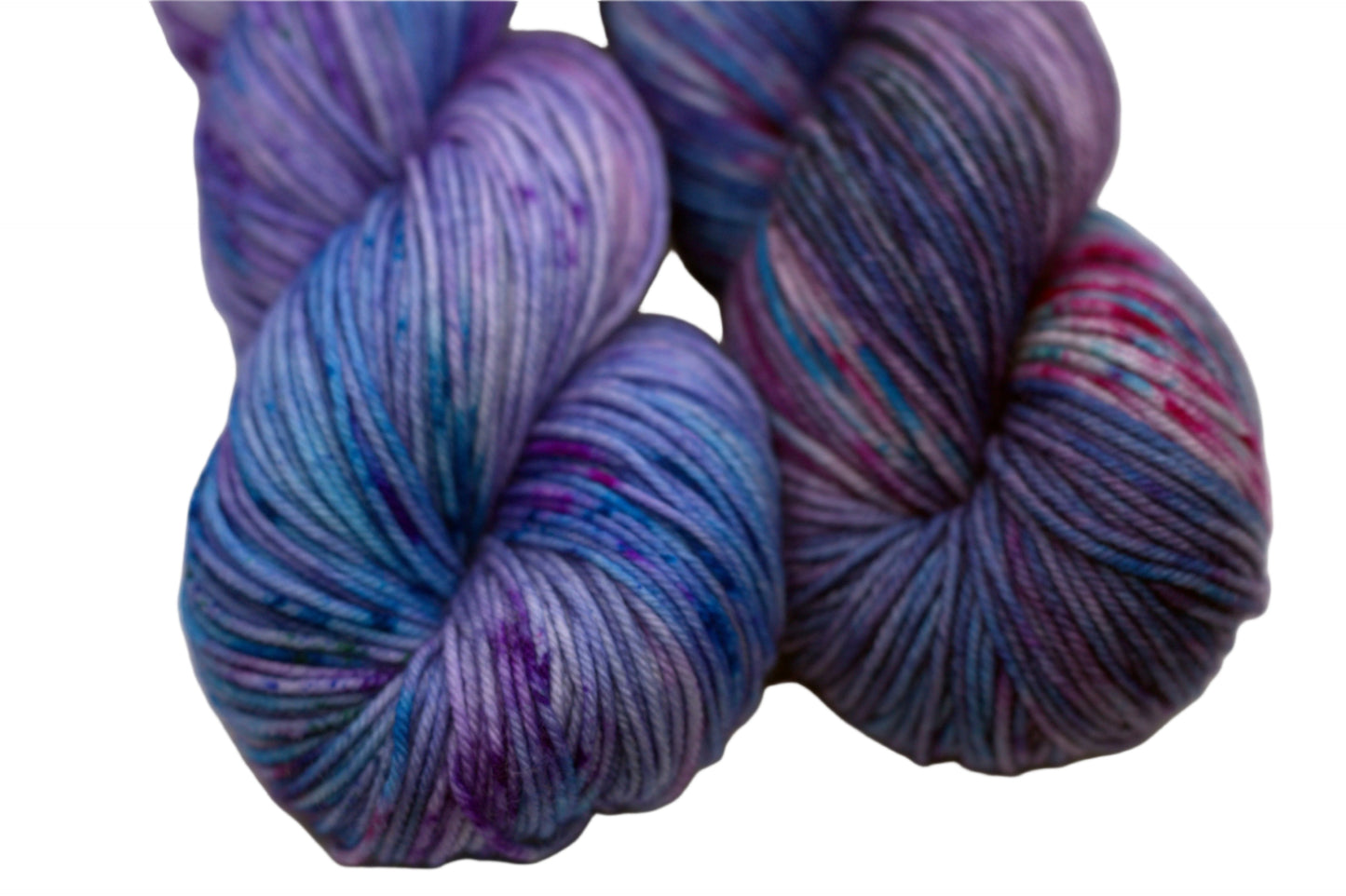 close up of two twisted skeins light purple yarn with turquoise, magenta and black speckles on white background.