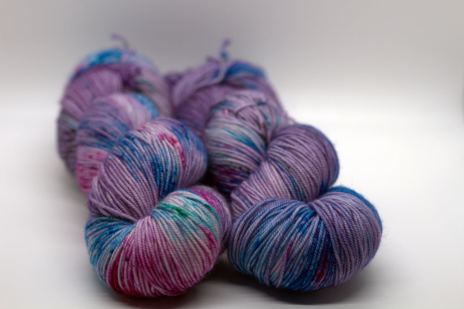 Two twisted skeins of light purple yarn with turquoise, magenta and black speckles on white background.