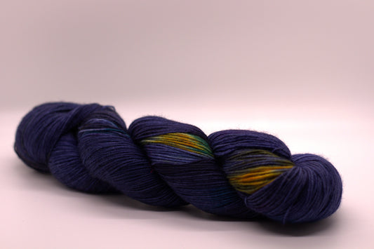 one twisted skein navy blue, yellow and green variegated yarn on white background.