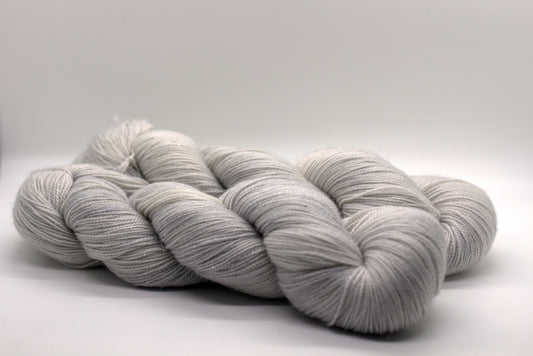 Two twist skeins of pale tonal silver yarn on white background