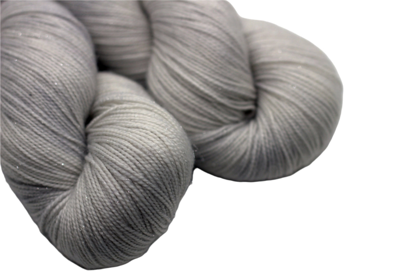 Close up of two twisted skeins pale silver tonal yarn on white background.