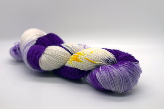 Twisted skein of Purple and white yarn with yellow and blue speckles on white background.