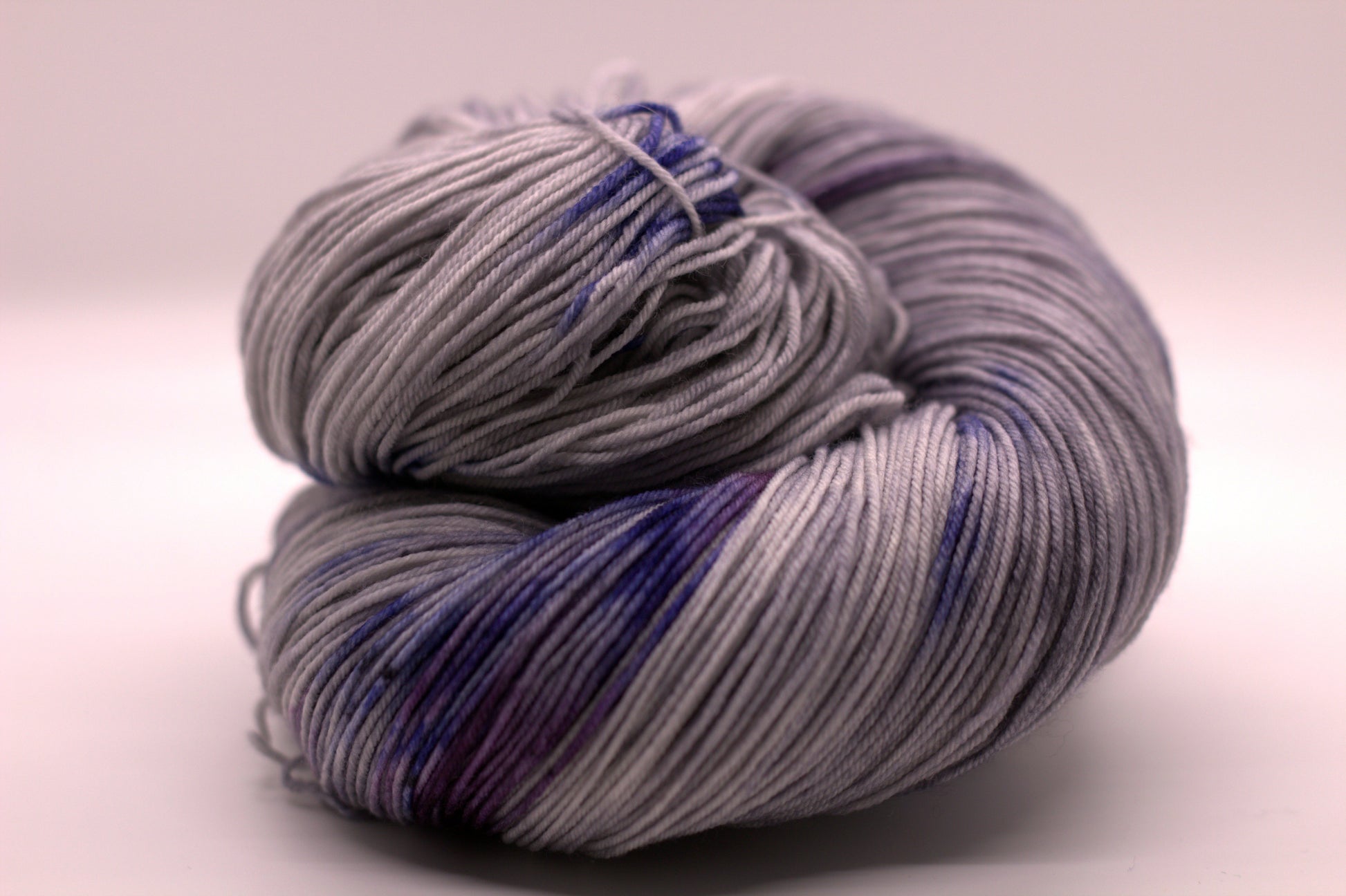 One curled skein of gray, blue and purple variegated yarn on white background.