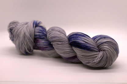 One twisted skein gray, blue and purple variegated yarn on white background.