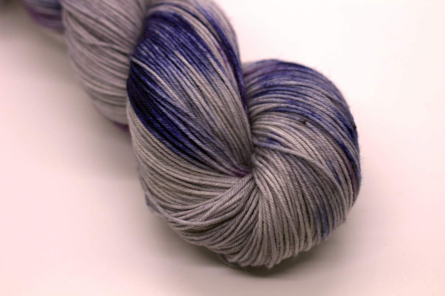 Close up of one twisted skein of gray, blue and purple variegated yarn on white background.