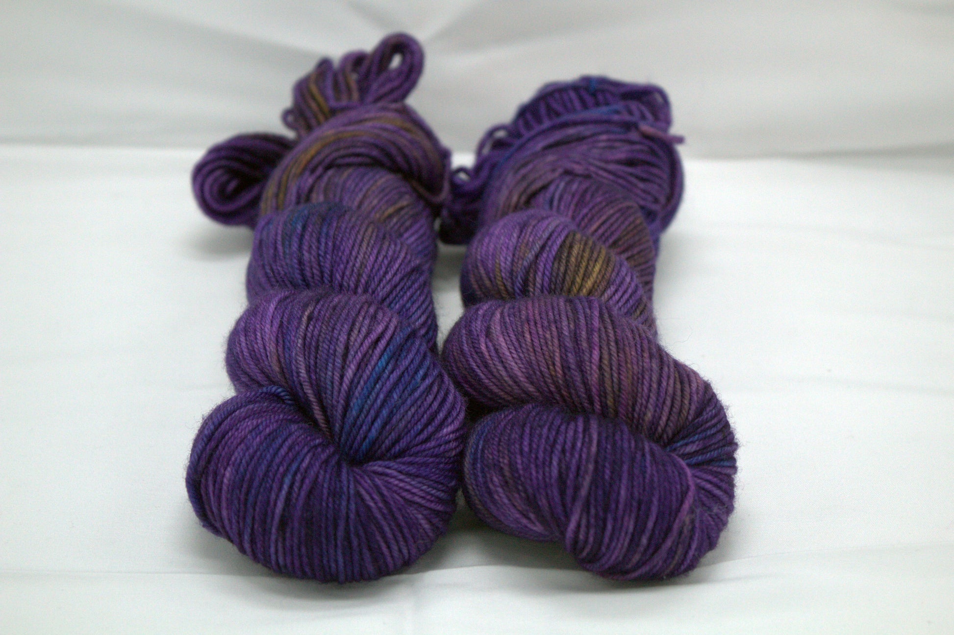 two twisted skeins variegated purple yarn on white background.