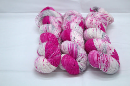three twisted skeins bright pink variegated yarn with pink and dark grey speckles on white background.