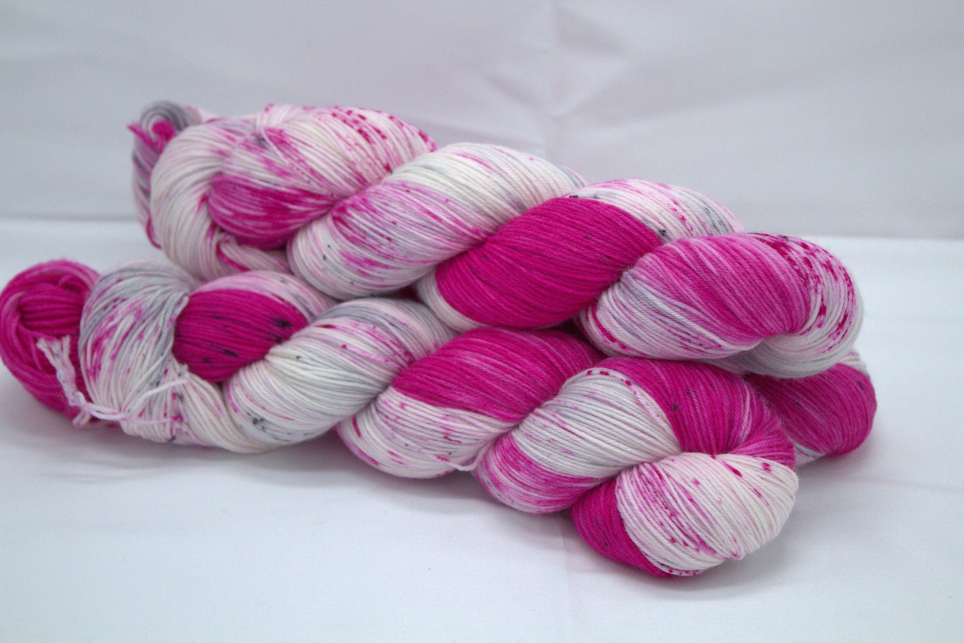 side view of three twisted skeins bright pink variegated yarn with pink and dark gray speckles on white background.