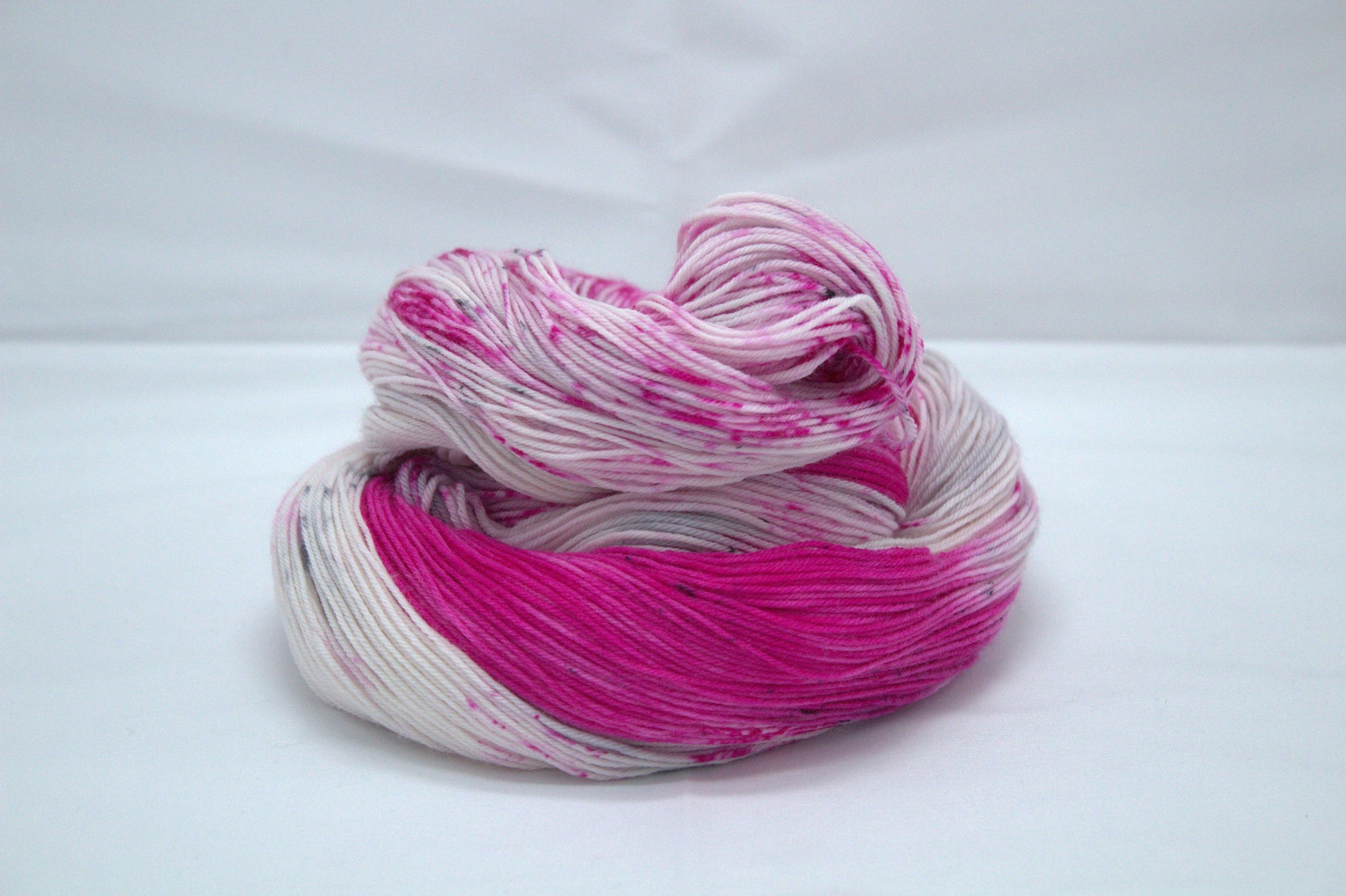 one curled up skein bright pink variegated yarn with pink and dark gray speckles on light background.