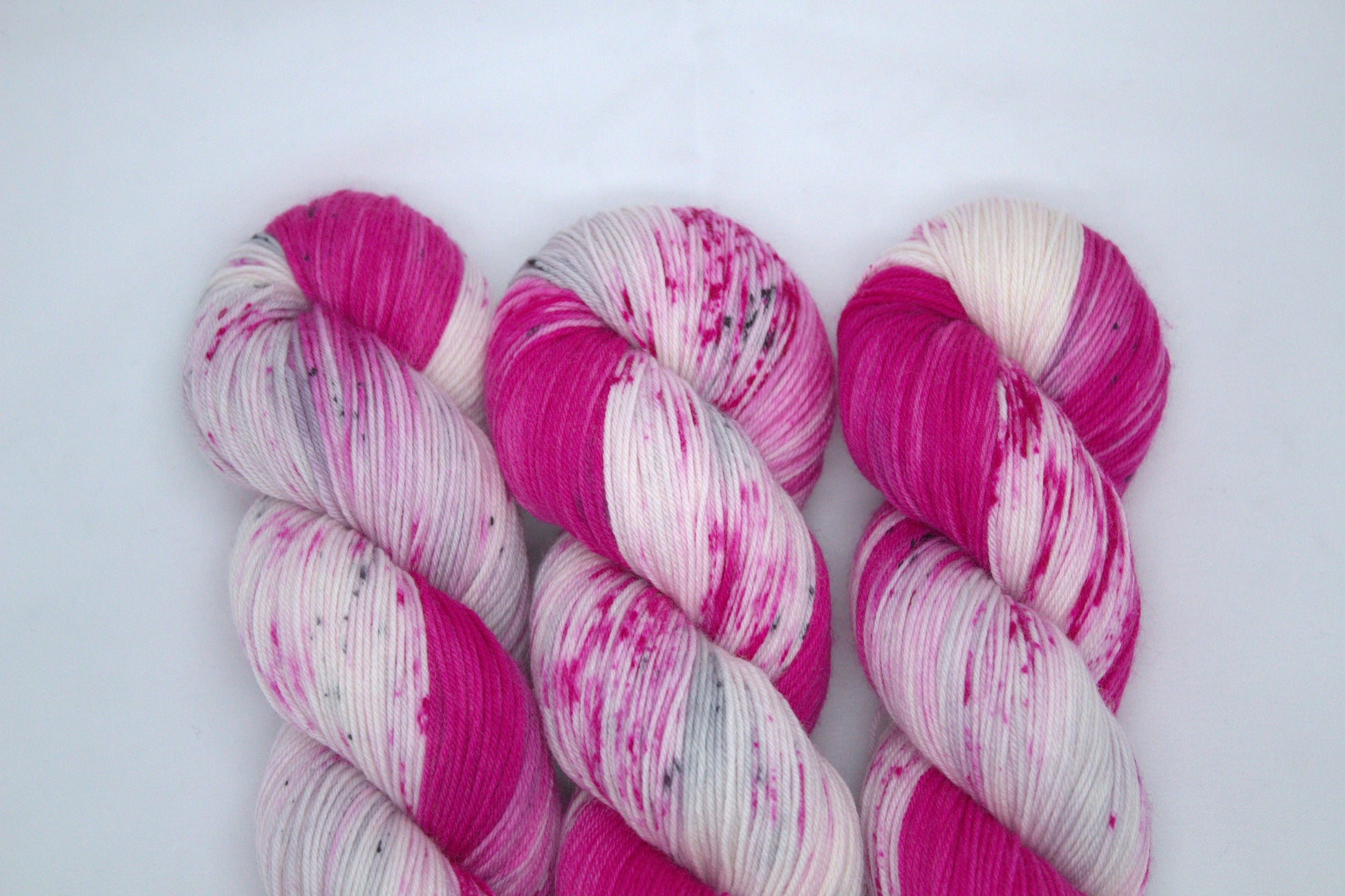 three twisted skeins bright pink variegated yarn with pink and dark gray speckles on white background.