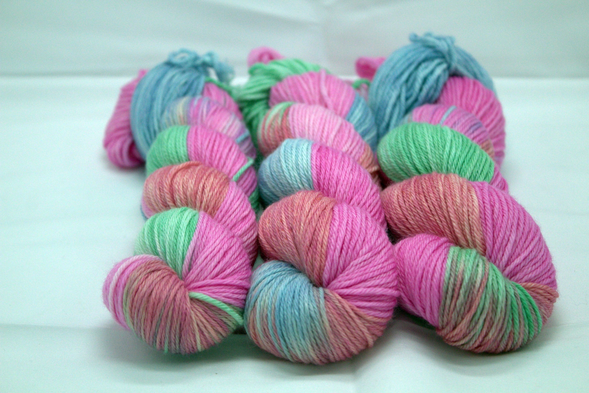 three twisted skeins variegated pinks, blue and green yarn on white background.