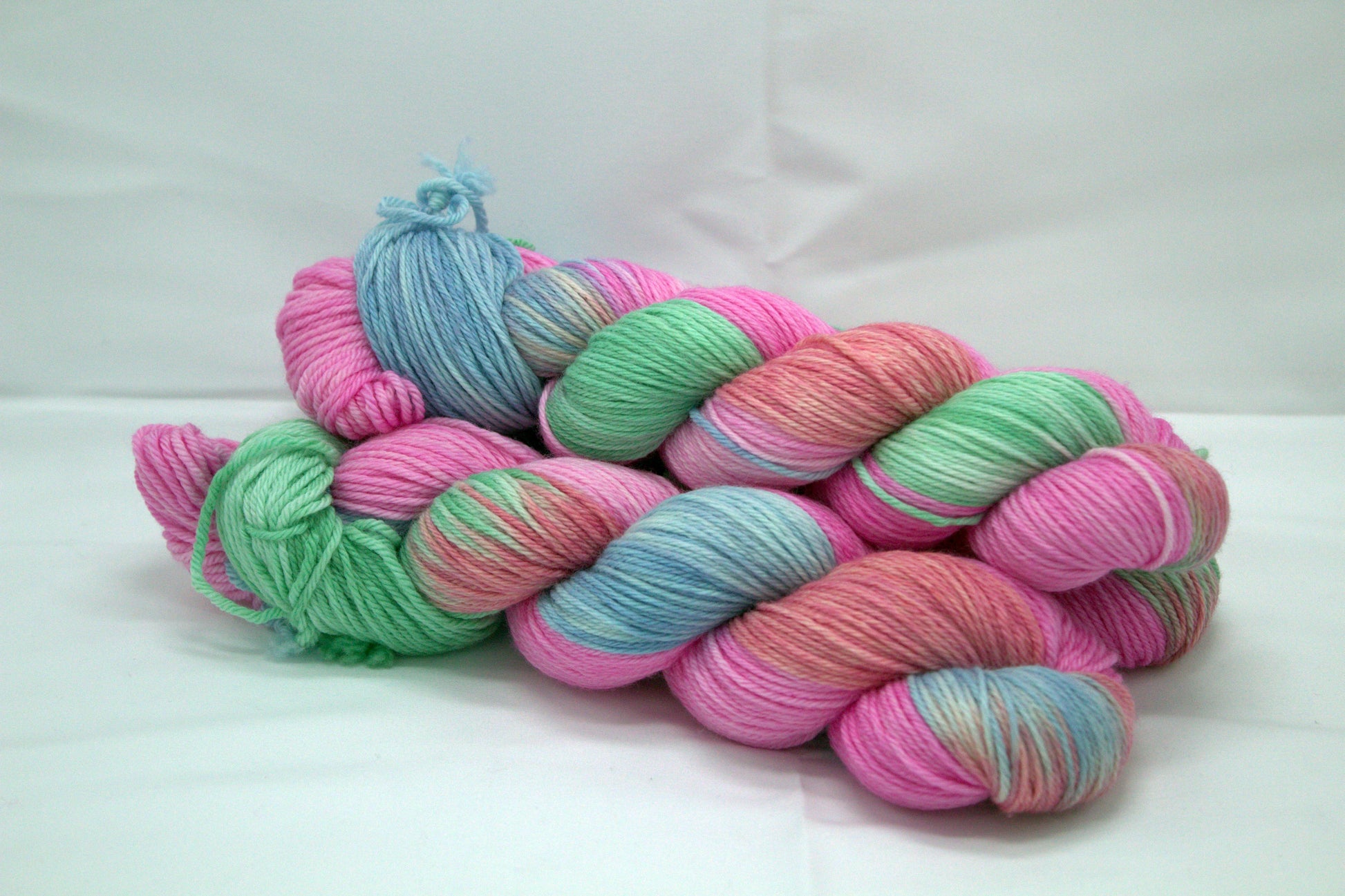 side view of three twisted skeins variegated pinks, blue and green yarn on white background.