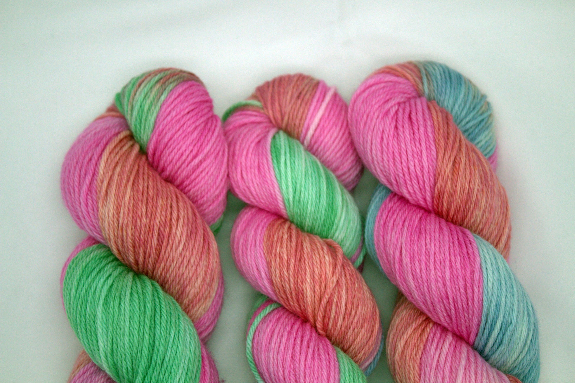 close up of three twisted skeins variegated pinks, blue and green yarn on white background.