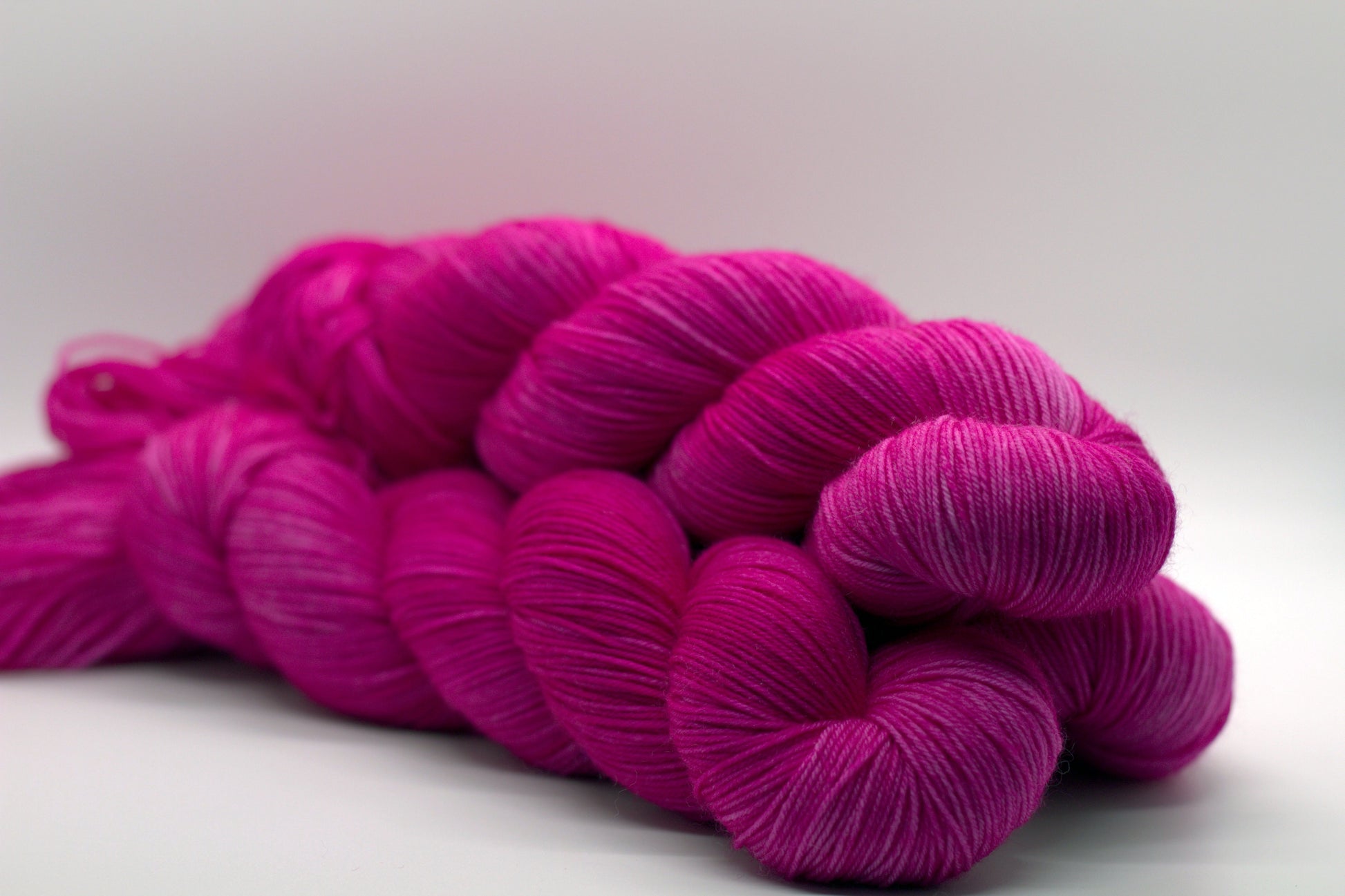 side view of three twisted skeins tonal bright pink yarn on white background.