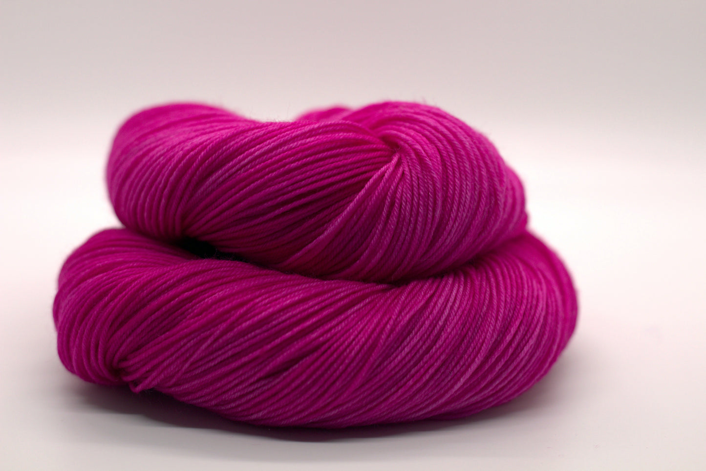 one curled up skein tonal bright pink yarn on white background. 