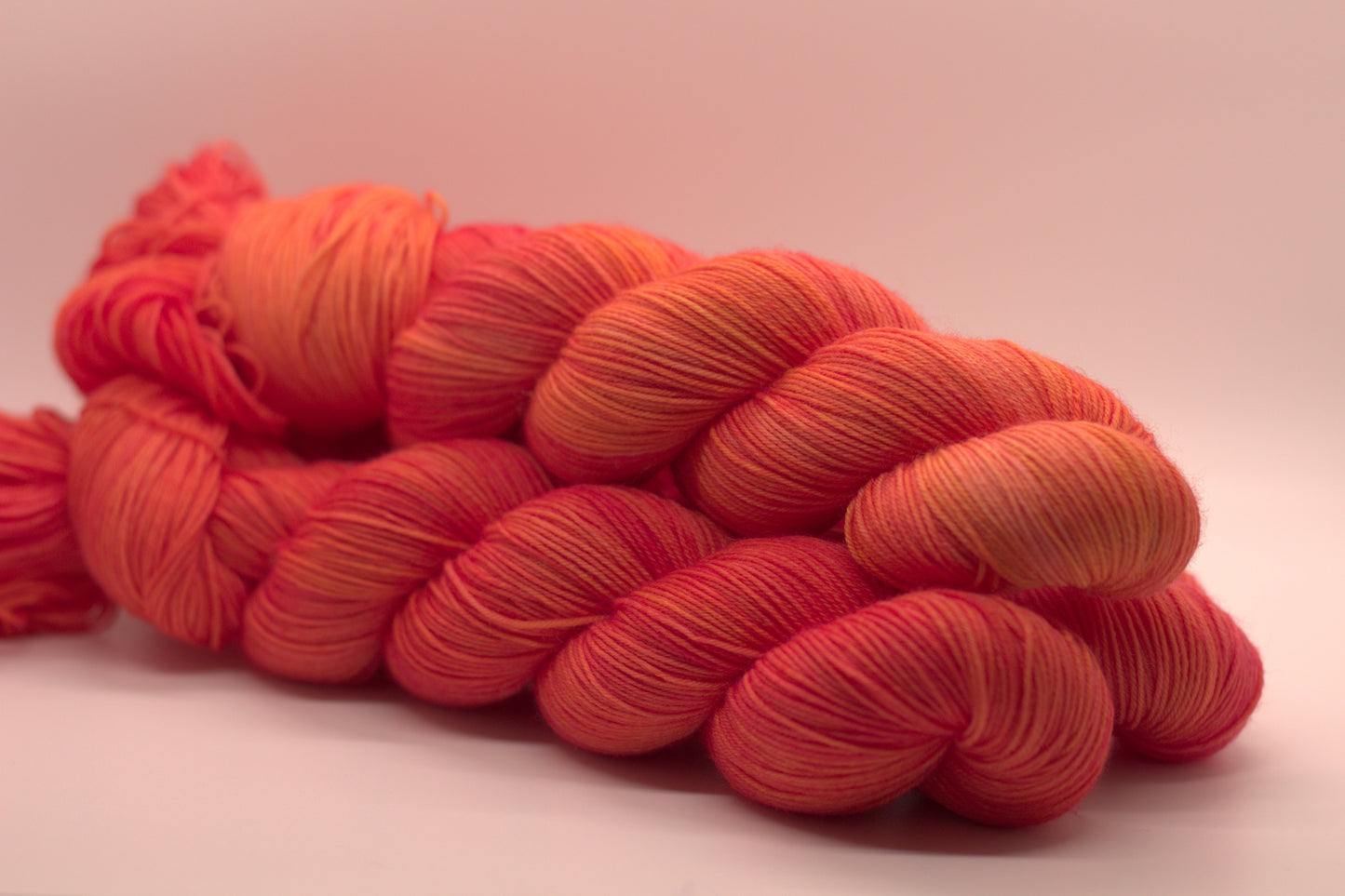 side view of three twisted skeins orange yarn with yellow undertones on white background.