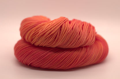 One curled skein of orange yarn with yellow undertones on white background.