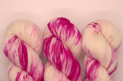 close up of three twisted skeins bright pink speckled yarn on white background.
