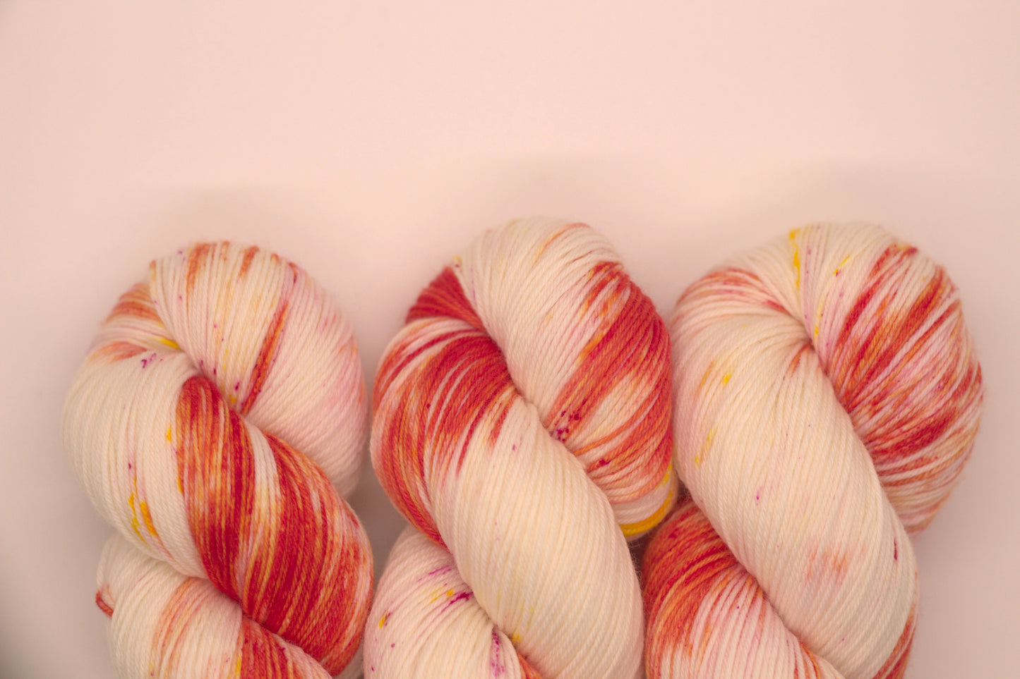 close up of three twisted skein orange, yellow and magenta speckled yarn on white background.