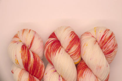close up of three twisted skein orange, yellow and magenta speckled yarn on white background.