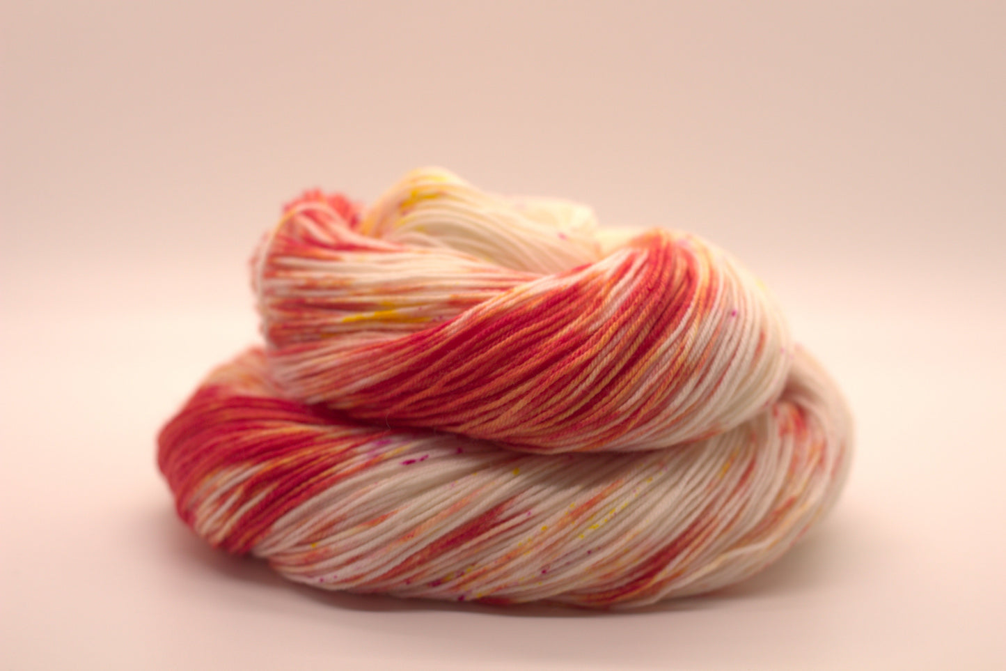 One curled skein orange, yellow and magenta speckled yarn on white background.