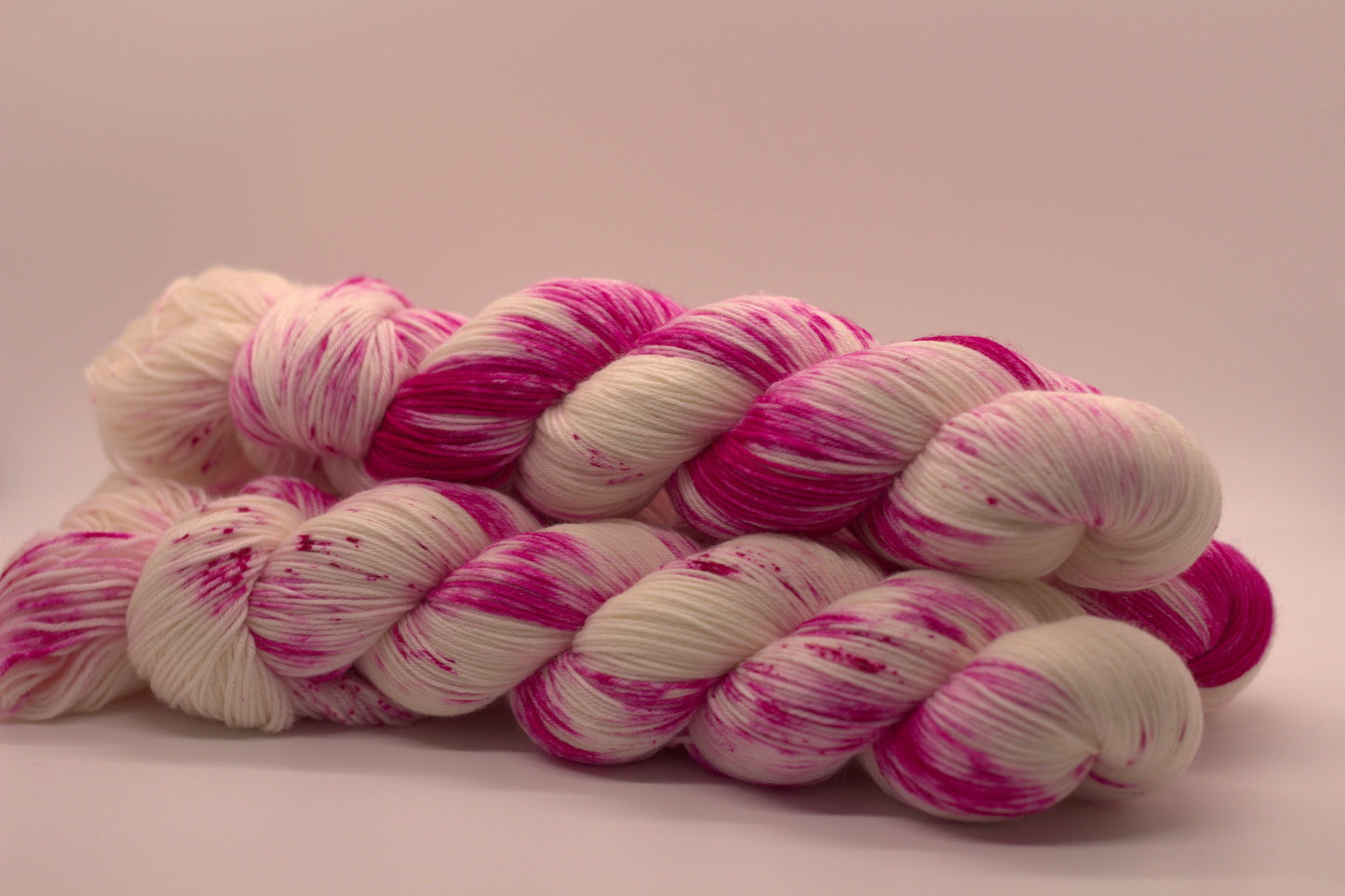 side view of three twisted skeins bright pink speckled yarn on white background.
