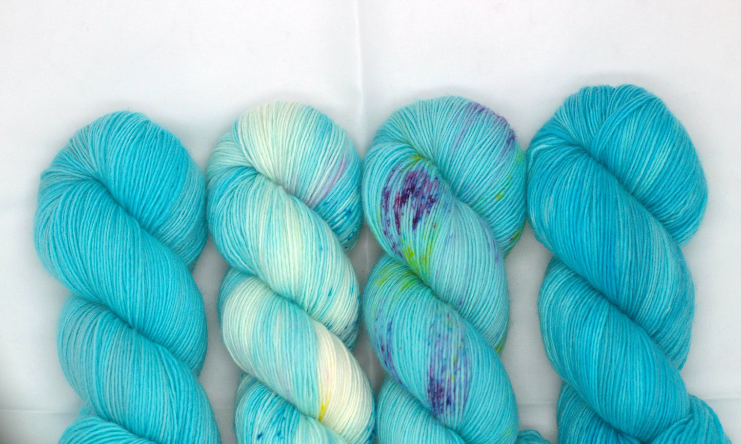 Four twisted complimentary skeins in varying shades of turquoise on white background.