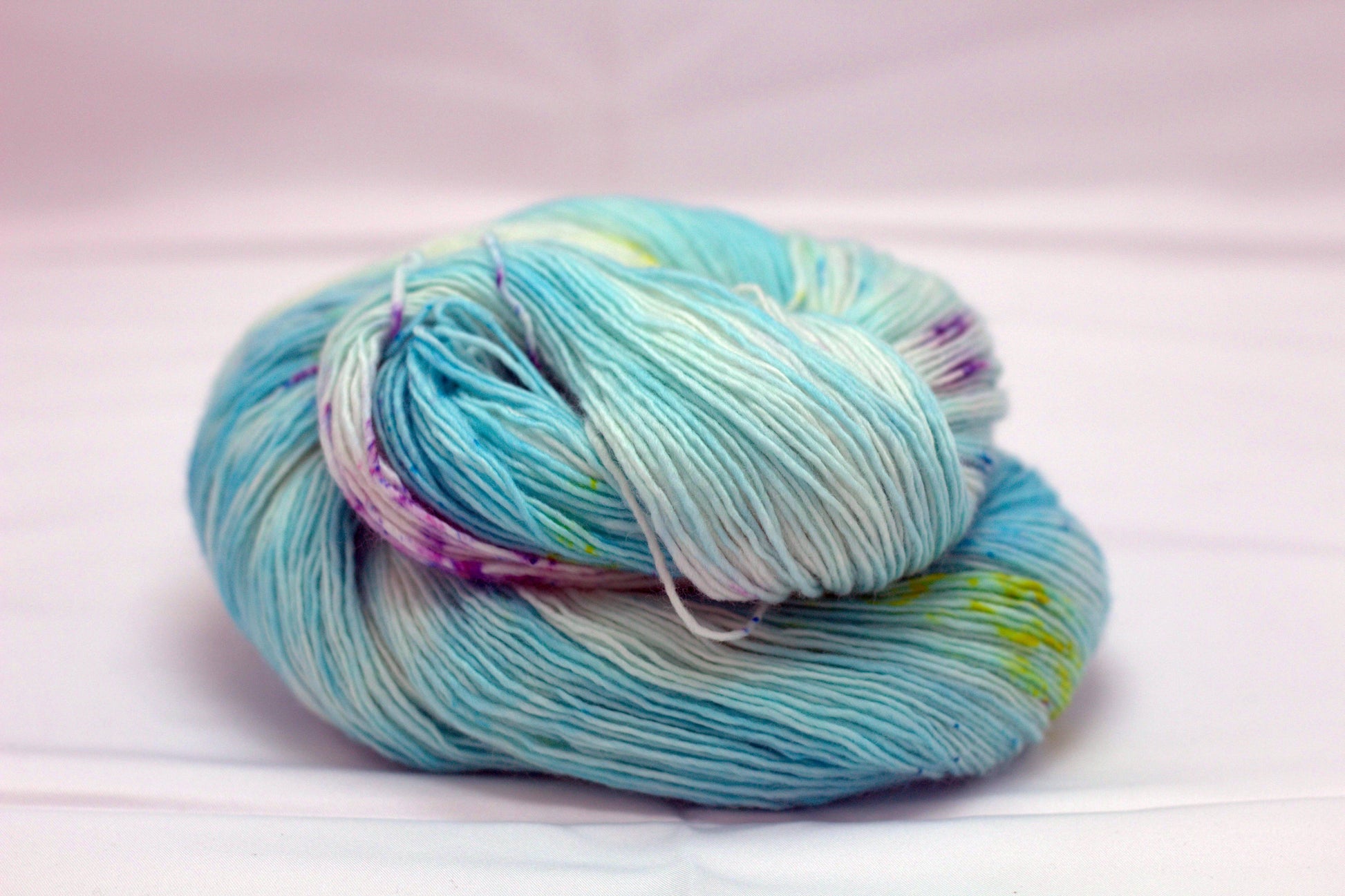 One curled skein of variegated turquoise and white yarn with yellow and purple speckles on white background.