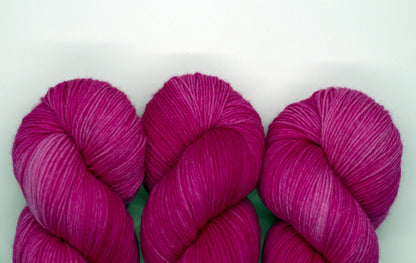 close up of three twisted skeins tonal bright pink yarn on white background.